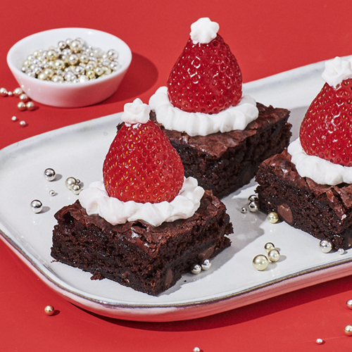 Brownies topped with whipped cream and strawberries to make Santa hats